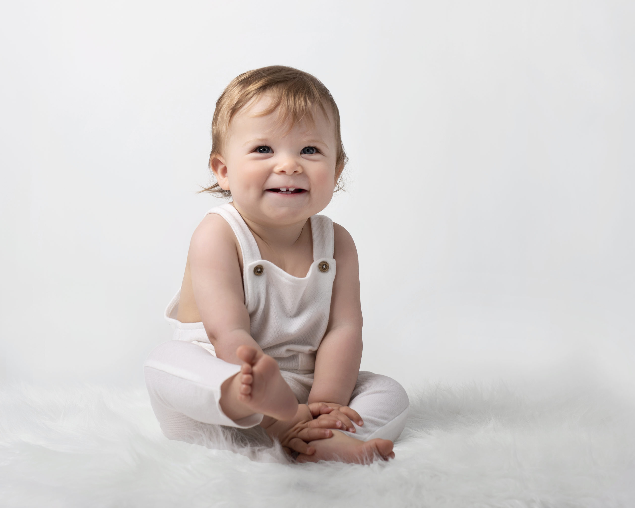 Cute baby boy sitting on white fur with a big smile by newborn photographer in folkestone and canterbury