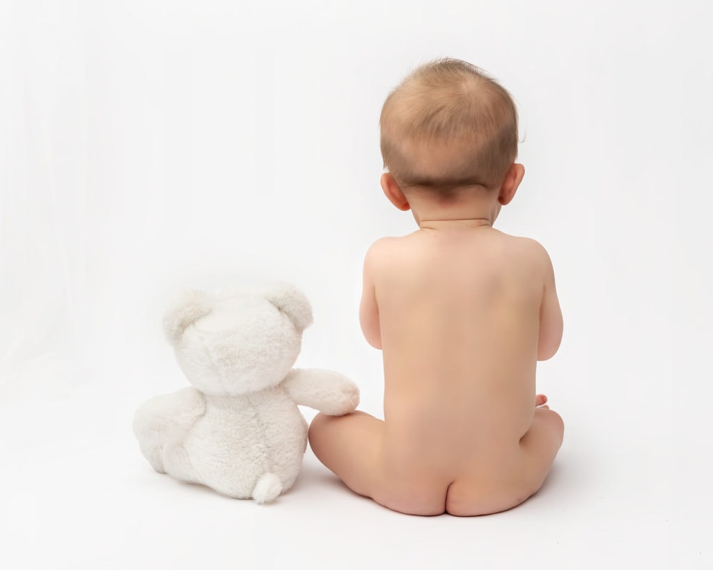 Baby facing away from the camera with a white teddy bear on a baby photography session n Kent