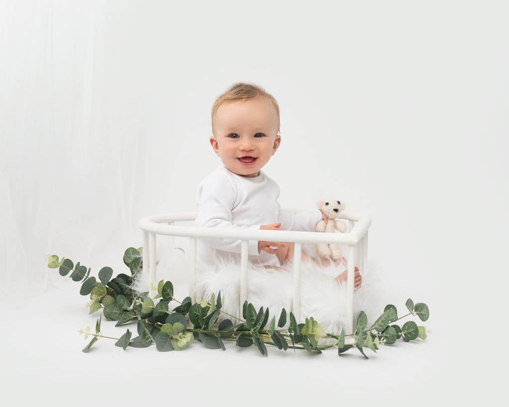 sitting baby in a wooden crib smiling on a baby photoshoot in Kent