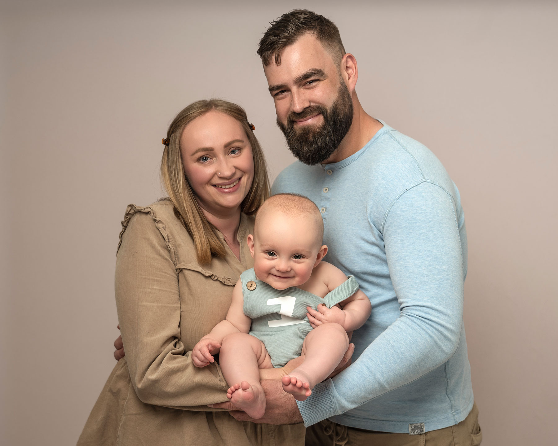 mum dad and baby boy smiling at the camera on a cake smash photoshoot in Kent