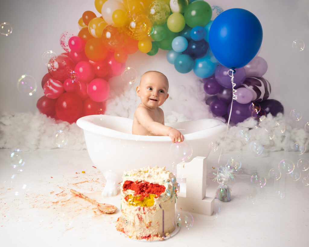 baby boy sitting in a bath with rainbow balloons and cake on a cake smash photoshoot in Canterbury